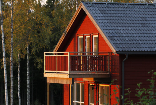 Röd stuga omgiven av skog i kvällsljus.