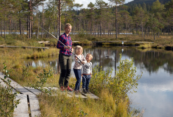 Mamma fiskar med två barn vid tjärn.