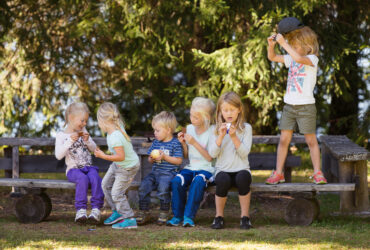 Flera barn sitter på enbänk och fikar.