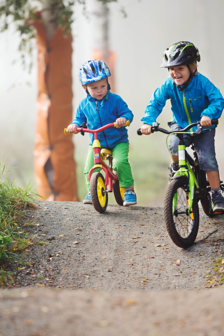 Små pojkar cyklar mtb och kick bike på terrängbana.
