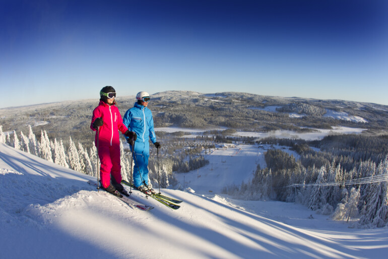 Par står på skidor på toppen av backen.