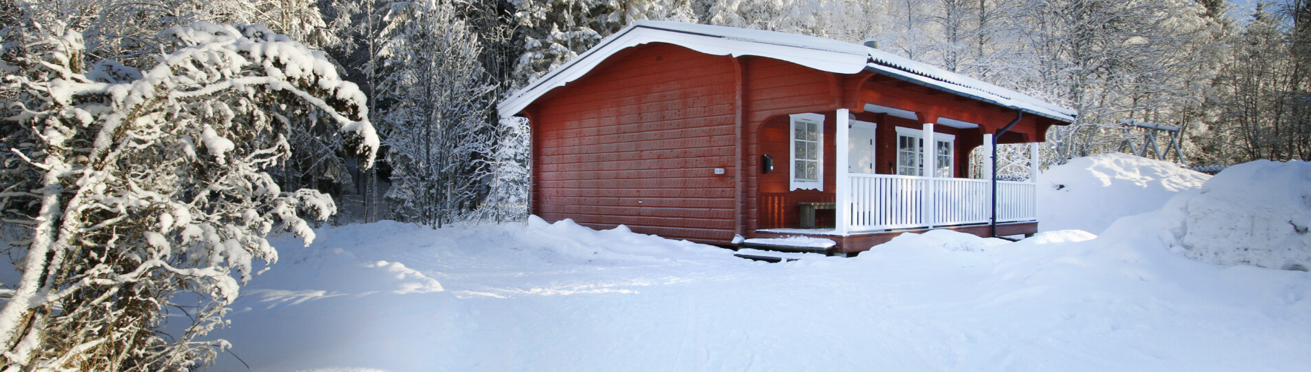 Röd stuga med vita knutar i vinterlandskap.