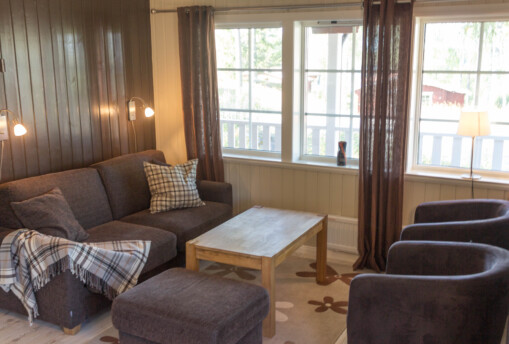 Vardagsrum med tvåsittssoffa, fåtöljer och sittpuff i sommarstuga.