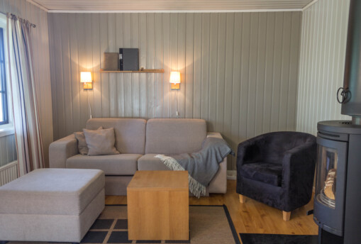 Vardagsrum med hel träpanel vägg, soffa och fåtölj i stuga.