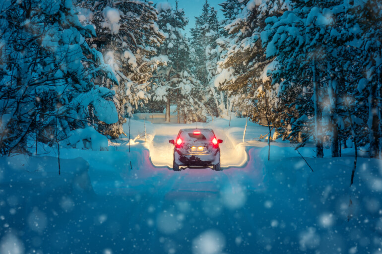 Bil kör genom snölandskap.