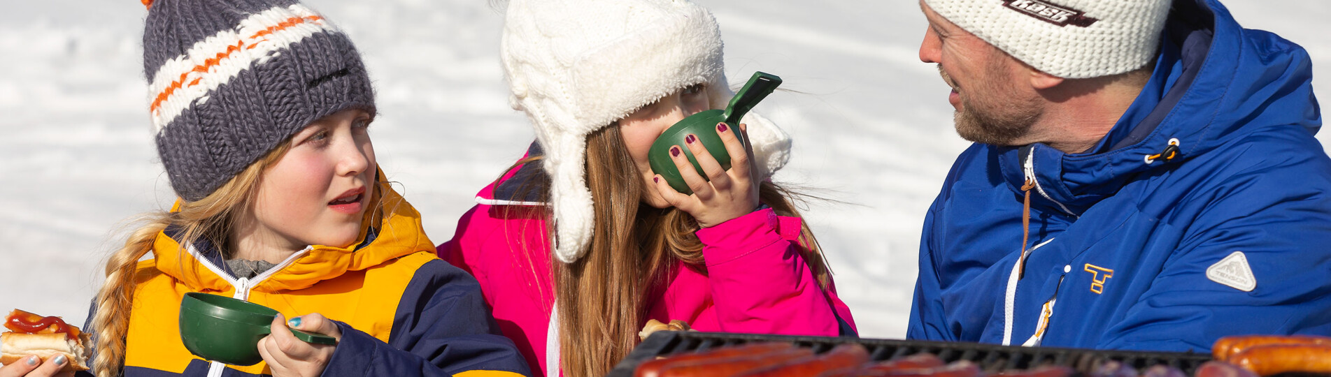 Familj grillar korv utomhus vid en grillplats i skidbacken