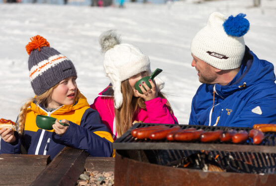 Familj grillar korv utomhus vid en grillplats i skidbacken