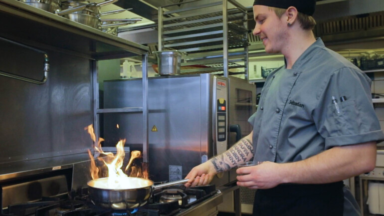 En kock på Säfsen lagar mat på spisen och flamberar