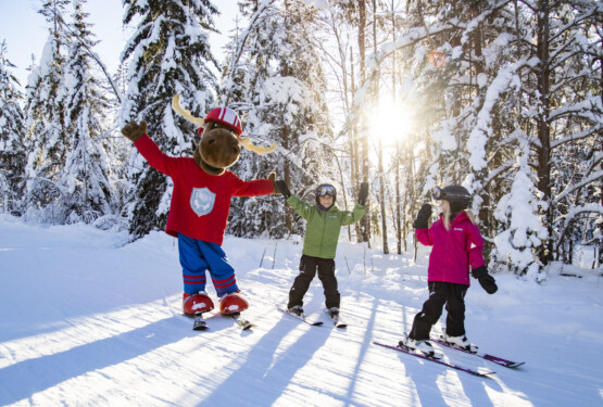 Älgen Filurius med barn i en solig skidbacke