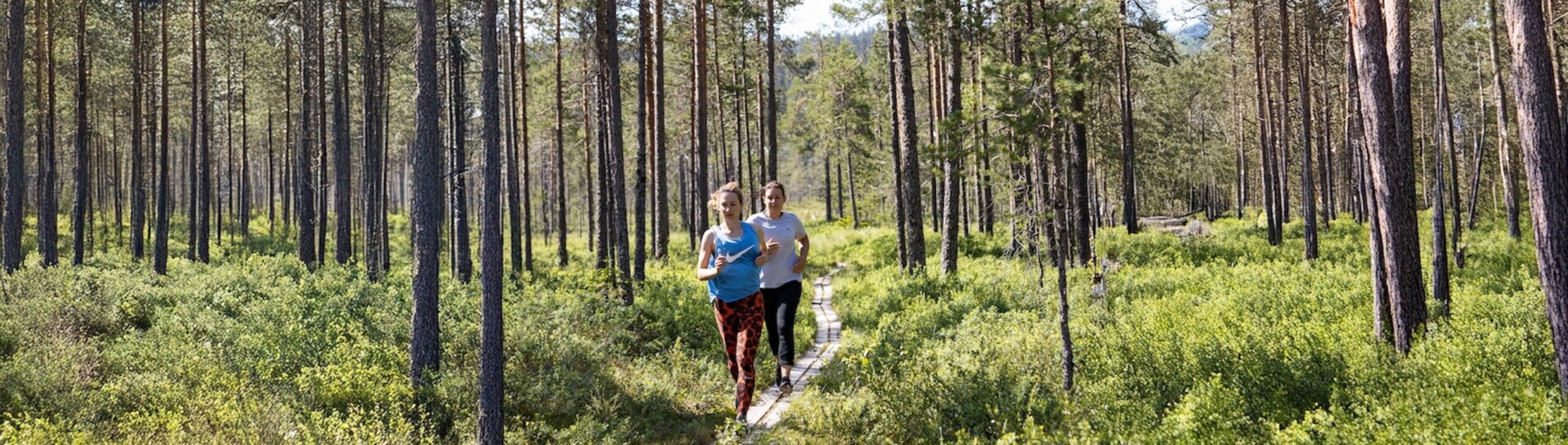 två kvinnor som springer över en spång i skogen