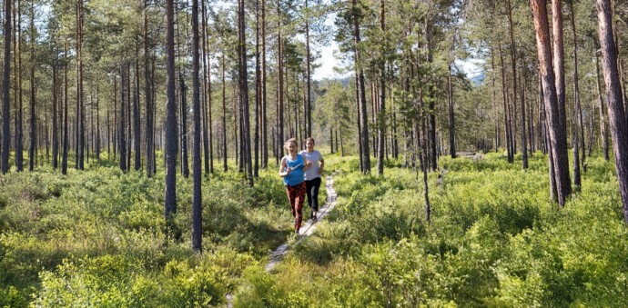 två kvinnor som springer över en spång i skogen