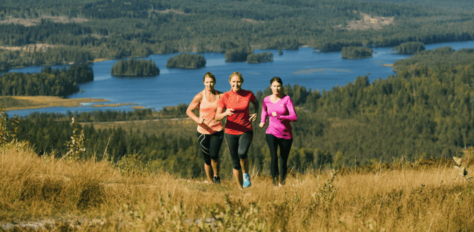 tre personer springer uppför en backe med skog och sjö i bakgrunden